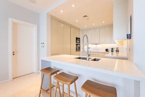 A modern kitchen with a white countertop, stainless steel sink, and wooden stools.