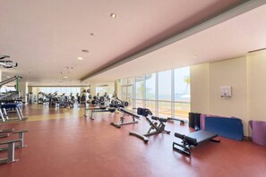 Ein geräumiges Fitnessstudio mit verschiedenen Trainingsgeräten, großen Fenstern und Blick ins Freie.