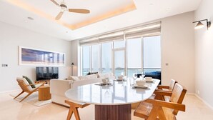 Uma sala de estar moderna com uma mesa redonda grande posta para refeições, um sofá e uma televisão.
