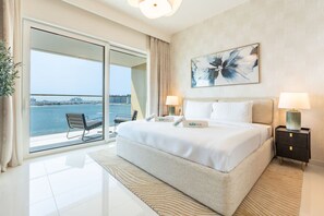 Ein modernes Hotelzimmer mit einem großen Bett, zwei Nachttischen und Blick auf das Meer sowie eine Stadtkulisse im Hintergrund.
