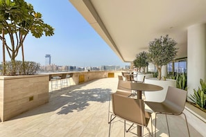 A rooftop terrace with seating and plants, overlooking a cityscape.