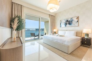 A modern hotel room with a large bed, two bedside tables, a view of the sea, and a balcony with chairs.