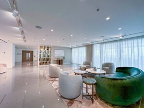 Amplia sala de estar con diseño moderno, que incluye un sofá verde, diversas opciones de asiento y un gran ventanal con cortinas.