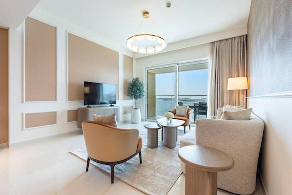 A modern hotel room with a large TV, comfortable seating, a small table, and a view of the city.