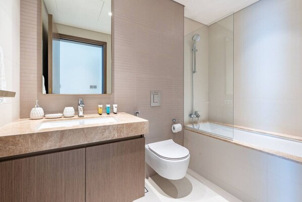 A modern bathroom with a marble countertop, a large mirror, a toilet, and a glass-enclosed shower area.