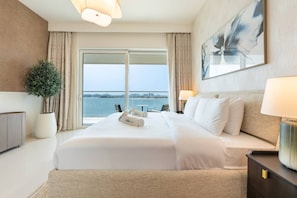 A hotel room with a large bed, a potted plant, a view of the water, and a painting on the wall.