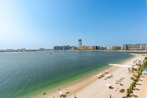 Un paisaje urbano costero con una playa de arena, aguas azules cristalinas y modernos rascacielos al fondo.