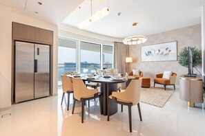 A modern dining area with a round table, chairs, and a large window offering a city view.