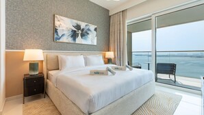 Une chambre d’hôtel moderne avec un grand lit, deux tables de chevet avec des lampes, une grande fenêtre donnant sur la mer et un tableau au mur.