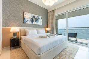 Een moderne hotelkamer met een groot bed, twee nachtkastjes met lampen, een groot raam met uitzicht op zee, en een schilderij aan de muur.