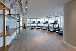 A modern gym with multiple treadmills, wooden flooring, and large windows offering views of the outdoors.