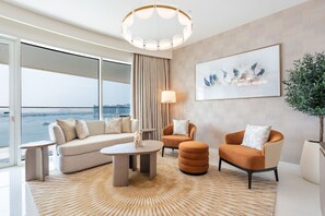A modern living room with a sofa, two armchairs, a coffee table, and a large window overlooking a body of water.
