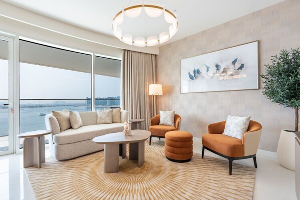 A modern living room with a sofa, two armchairs, a coffee table, and a large window overlooking a body of water.