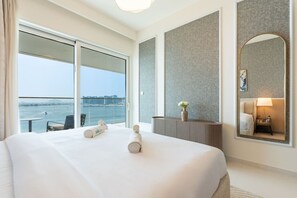 A hotel room with a large bed, a desk, a chair, a view of the water, and a cityscape.