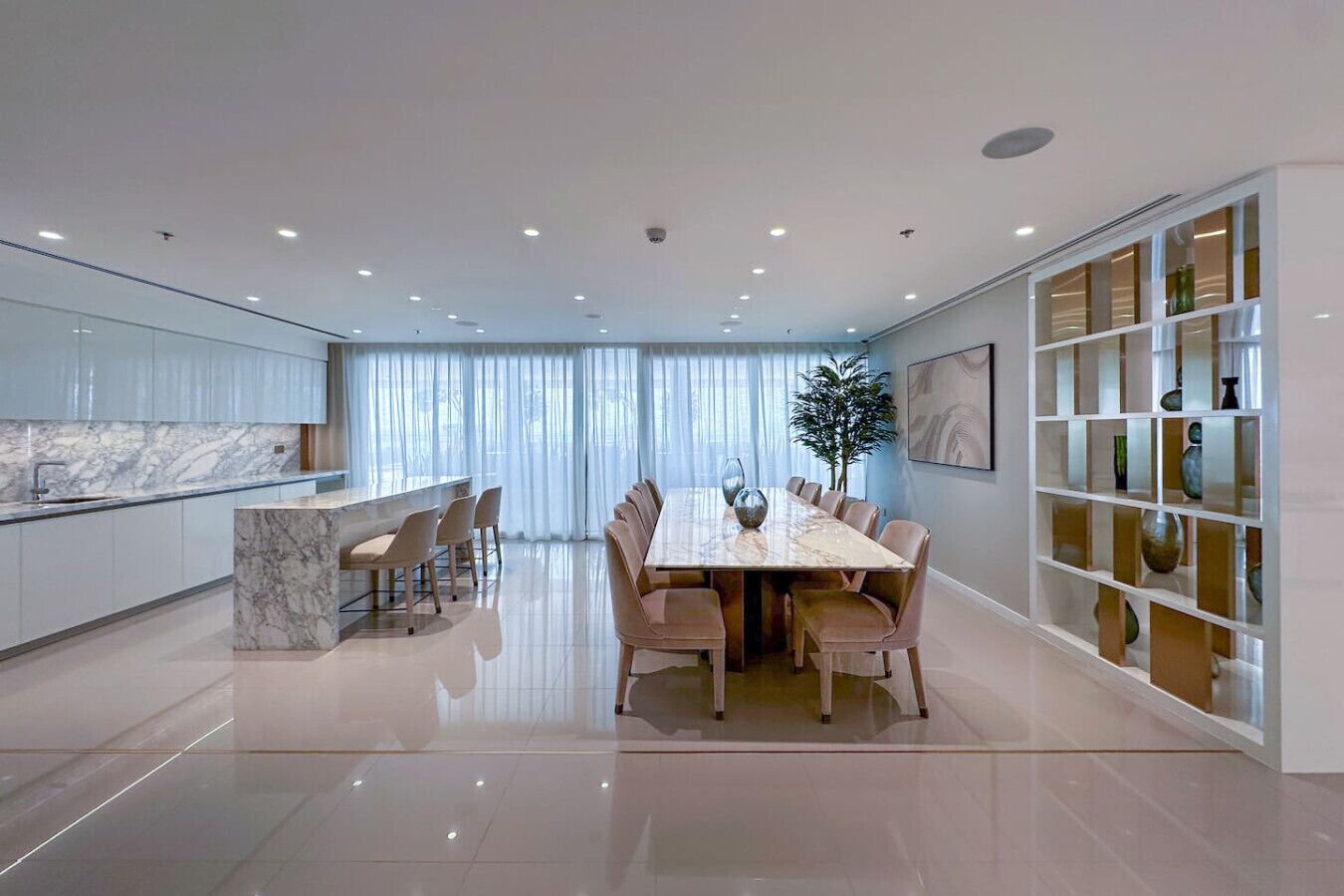 Una cocina moderna con encimera de mármol, una zona de comedor con mesa de mármol y un aparador de vidrio.