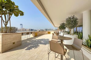 A rooftop terrace with seating and plants, overlooking a cityscape.