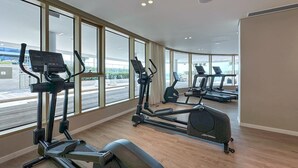 Une salle de sport moderne équipée de nombreux tapis de course et d’appareils elliptiques, et dotée de grandes fenêtres offrant une vue sur l’extérieur.
