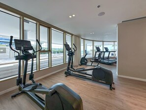 Un gimnasio moderno con múltiples cintas de correr y elípticas, con grandes ventanales que ofrecen vistas al exterior.