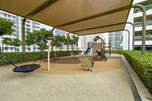 Un parque infantil al aire libre con columpios, toboganes y estructuras para escalar, rodeado de vegetación y edificios modernos.