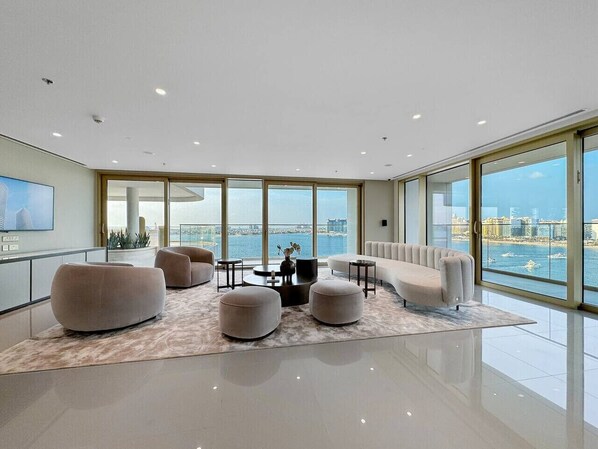 A spacious living room with a large window, a sofa, ottomans, and a coffee table.