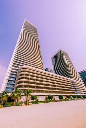 Un hotel moderno de gran altura con fachada curva, múltiples balcones y un área frontal ajardinada con palmeras.