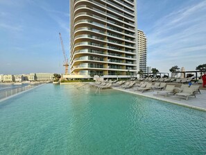 A modern hotel with a pool area, a crane, and a beach in the background.