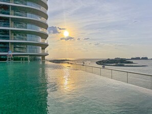A waterfront hotel with a pool and a view of the sunset over the water. - Chic 2 bedroom w Sunset and Palm Jumeirah Views (Dubai)