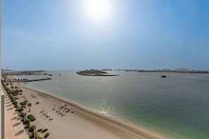 A coastal beach with clear waters, a sandy shore, and a promenade with umbrellas.