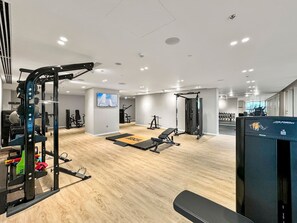 Un gimnasio moderno con suelo de madera, equipamiento de levantamiento de pesas y una pantalla de televisión.