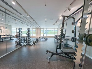 A gym with various exercise equipment, large windows, and a mirrored wall. - Chic 2 bedroom w Sunset and Palm Jumeirah Views (Dubai)