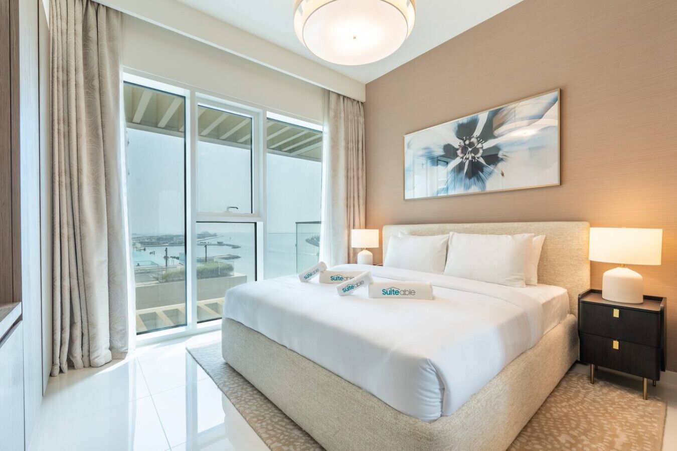 Habitación de hotel con una cama grande, dos lámparas de noche, vista a la ciudad y un cuadro en la pared.