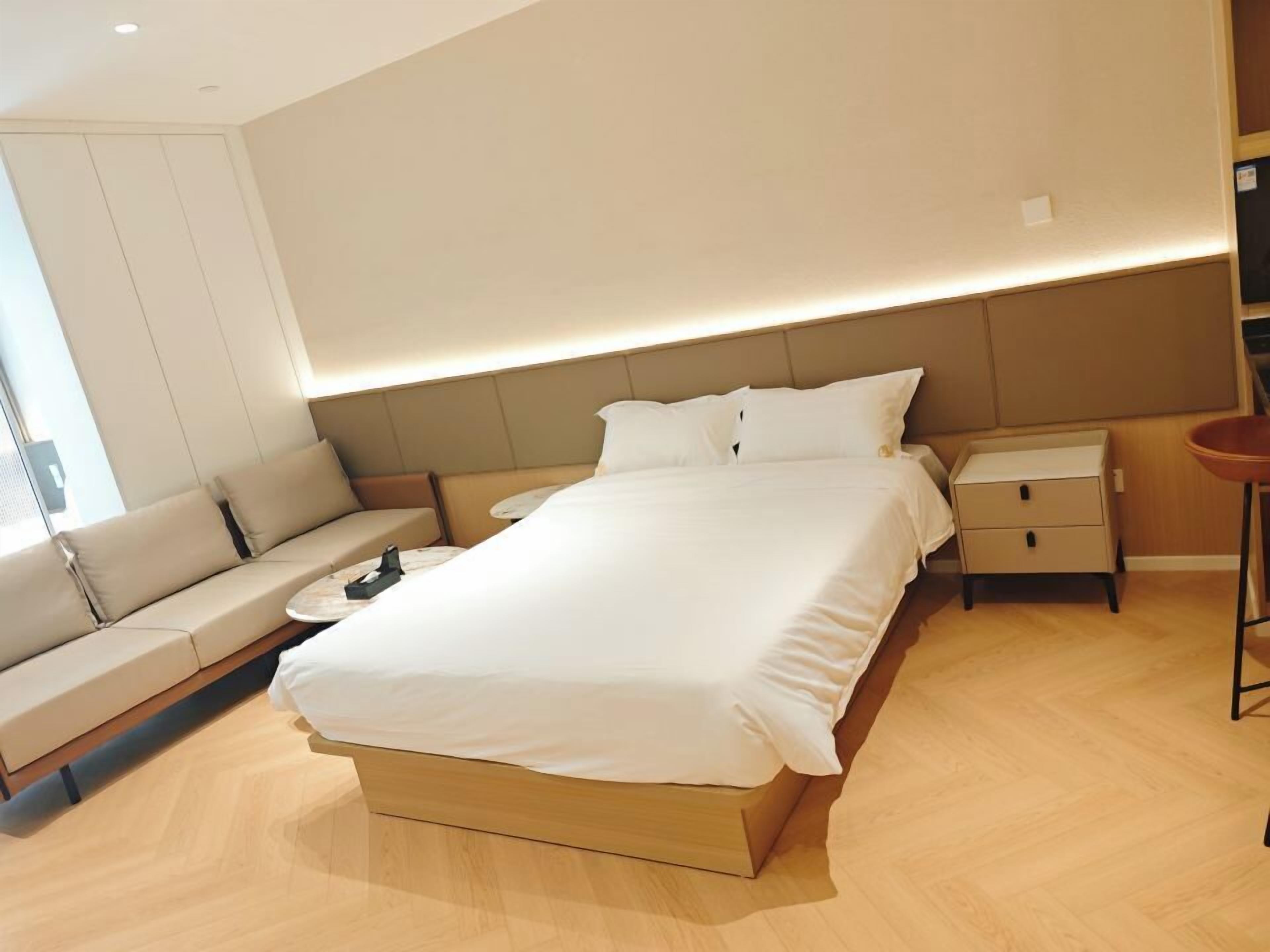 Una habitación de hotel moderna con una cama grande, un sofá, una mesita de noche y una mesilla.