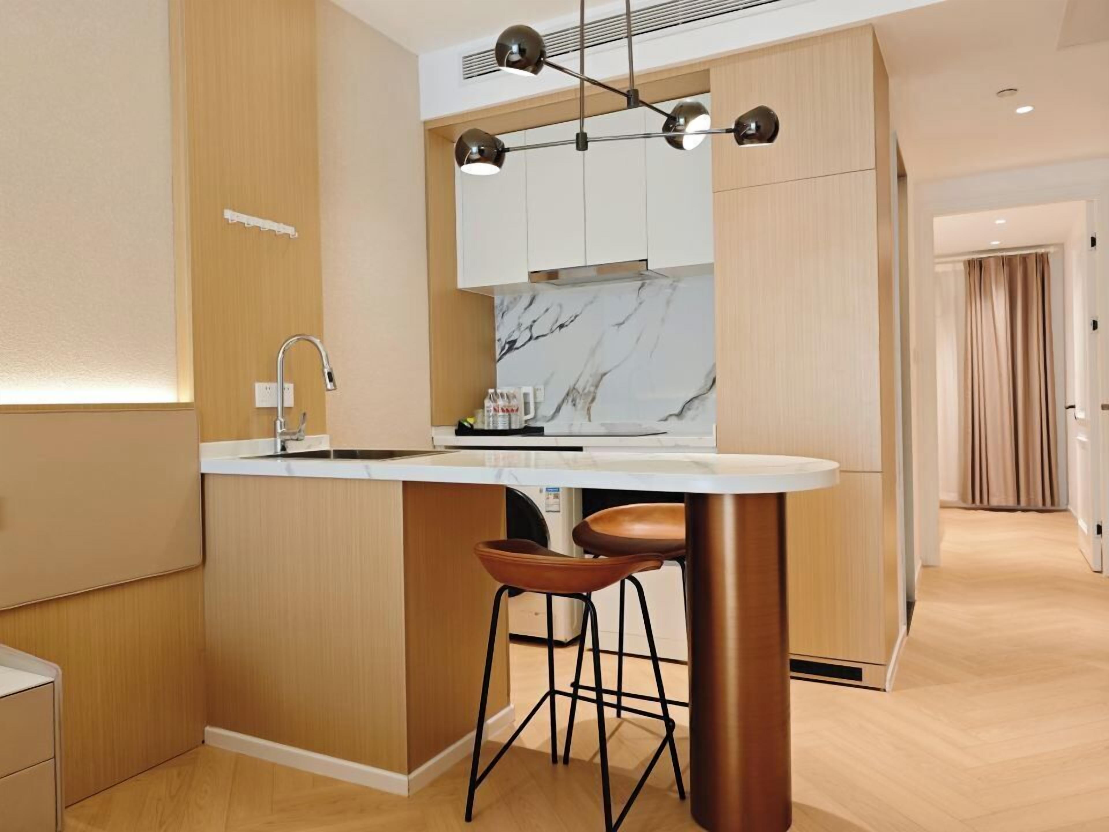 Una cucina moderna con schienale in marmo, mobili in legno, un'isola centrale con sgabelli e illuminazione a sospensione.