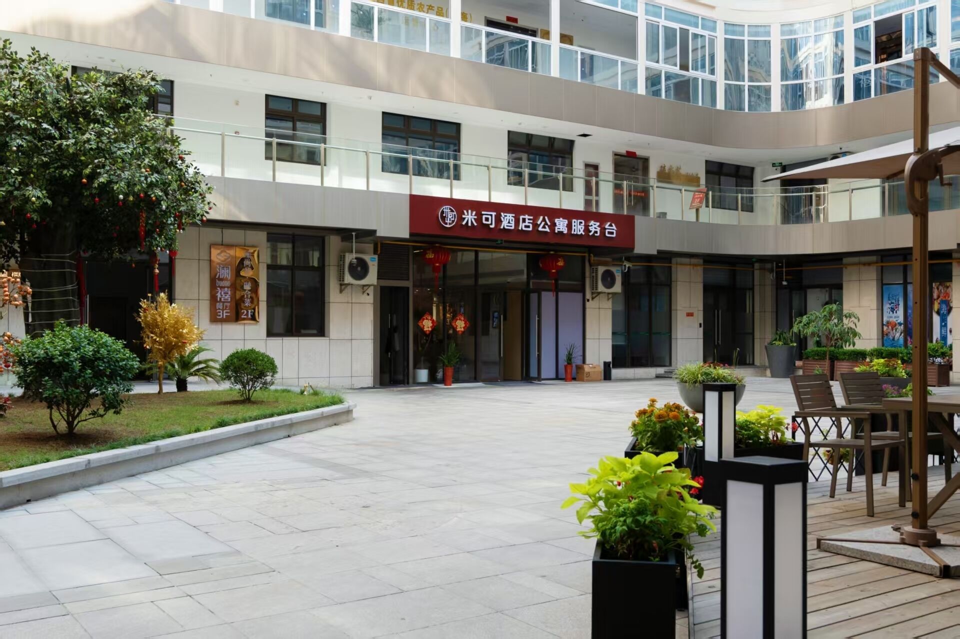 A hotel entrance with a red sign, outdoor seating, and potted plants.
