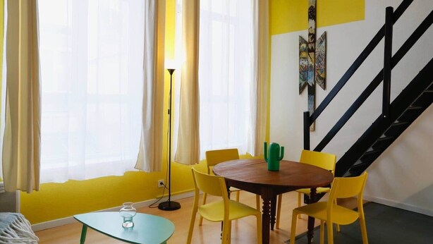A room with a wooden table, yellow chairs, a glass table, and a green cactus on the table. - Cosy, Old Lille, Unique, Neo-Vintage (Lille)