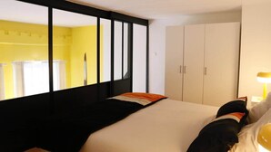 A hotel room with a bed, a wardrobe, and a mirror reflecting a yellow wall and a window with curtains. - Cosy, Old Lille, Unique, Neo-Vintage (Lille)