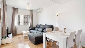 A modern living room with a grey sofa, a dining table with chairs, and a small white side table. - Beautiful 3-bedroom home in Playa Flamenca, Alicante. Spain. (Orihuela)