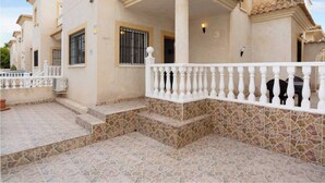 A multi-story residential building with a stone-tiled patio, white balustrades, and a central entrance with a decorative arch. - Beautiful 3-bedroom home in Playa Flamenca, Alicante. Spain. (Orihuela)