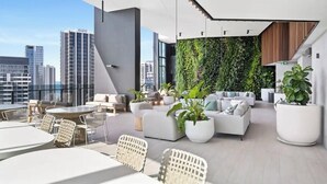 A modern rooftop lounge with white furniture, a green vertical garden wall, and a city skyline view.