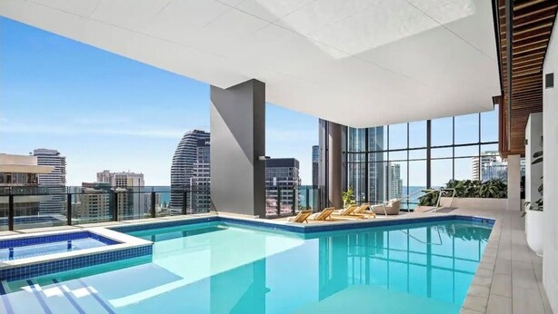 A rooftop pool with a city view, lounge chairs, and a modern architectural design.