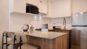 A modern kitchen with white cabinets, a stainless steel refrigerator, a granite countertop, and two bar stools. - w* | Chic 1BR Apartment in Miraflores (Lima)