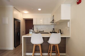 Une cuisine moderne avec des meubles blancs, un réfrigérateur en acier inoxydable et un îlot central doté de deux tabourets de bar.