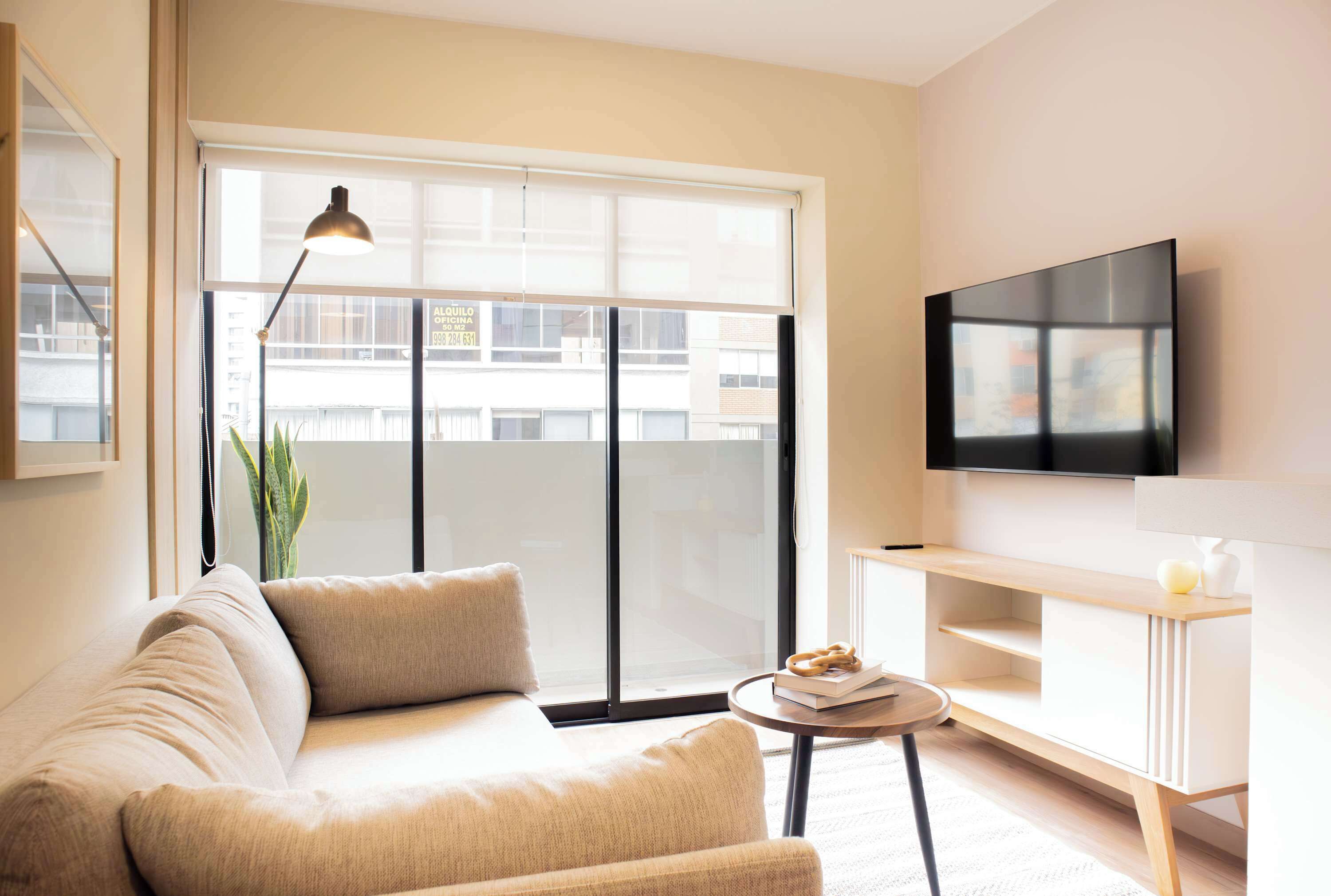 A modern living room with a sofa, a small table, a lamp, a TV, and a sliding glass door to the outside.