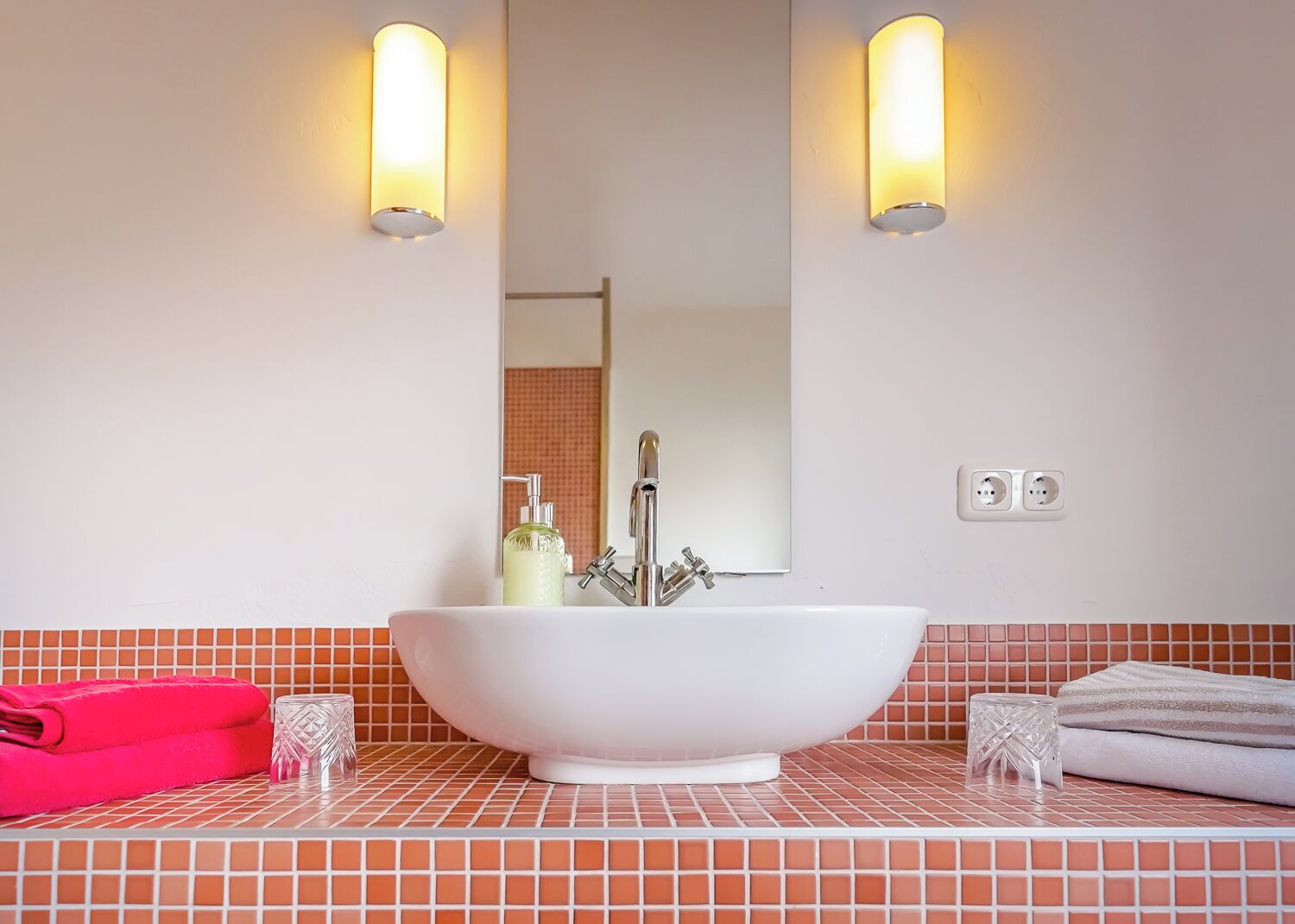 Un baño con un lavamanos blanco independiente, dos luces fijadas a la pared, un espejo y un salpicadero de azulejos.