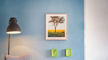 Ein Zimmer mit blauer Wand, einem gerahmten Bild von einem Baum, einer Lampe und zwei kleinen Bildern in grünem Rahmen.