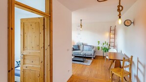 Eine Holztür führt in einen Wohnbereich mit einer Couch, einem Couchtisch und einer Pflanze.