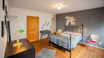 Een slaapkamer met een bed, een bureau, een stoel, een houten deur en een muur met afbeeldingen.