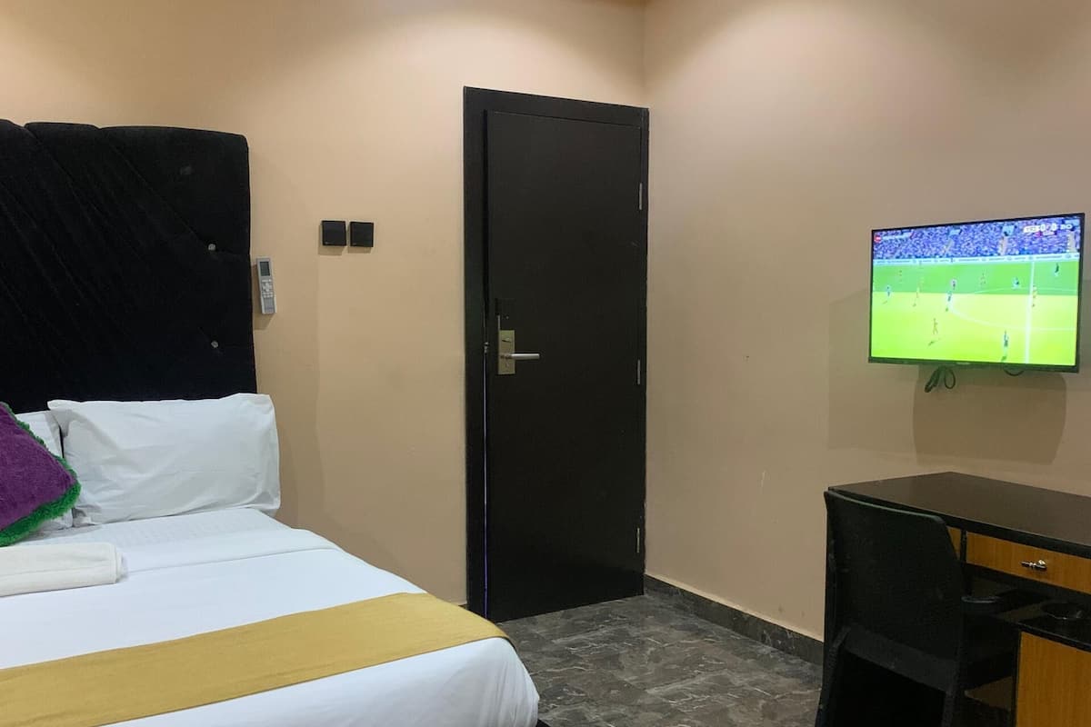 Una habitación de hotel con una cama, un escritorio, un televisor y una puerta.