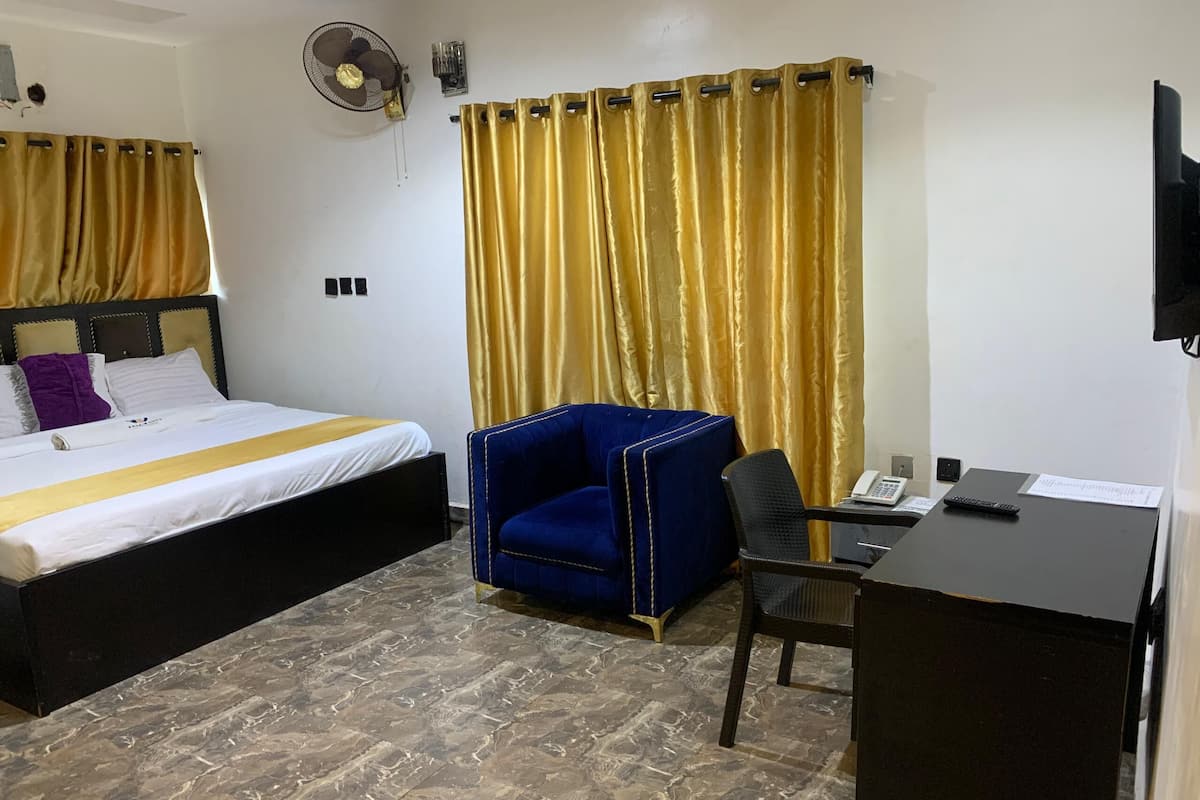 Una habitación de hotel con cama, escritorio, silla, ventilador y cortinas.