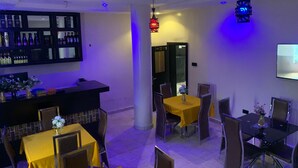 A restaurant with a bar area, tables with yellow tablecloths, and chairs.